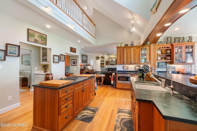 kitchen with light wood-type flooring, stainless steel appliances, sink, high vaulted ceiling, and an island with sink