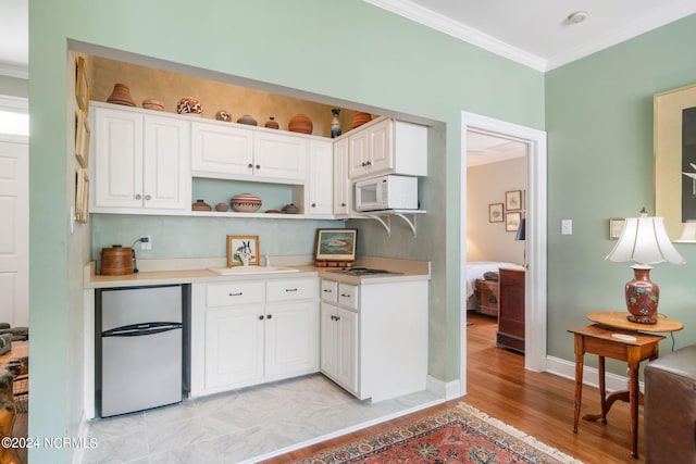 kitchen featuring white cabinets, sink, light wood-type flooring, ornamental molding, and stainless steel refrigerator