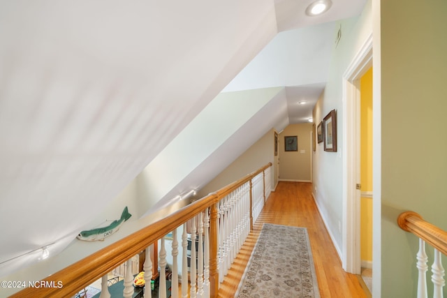 corridor with light wood-type flooring and vaulted ceiling