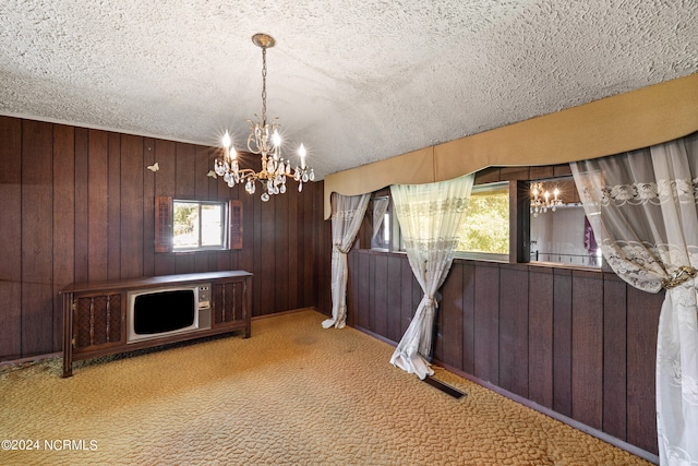 unfurnished dining area featuring wooden walls, light carpet, a textured ceiling, and an inviting chandelier