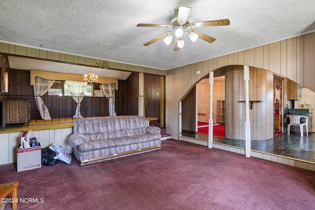 carpeted living room featuring ceiling fan with notable chandelier, a textured ceiling, and wooden walls