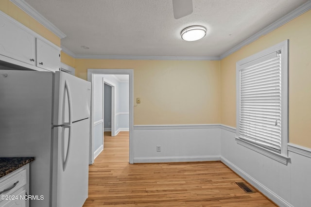 kitchen with white refrigerator, light wood-type flooring, crown molding, white cabinets, and a textured ceiling