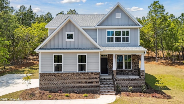 view of front of home featuring a shingled roof, board and batten siding, a porch, and brick siding