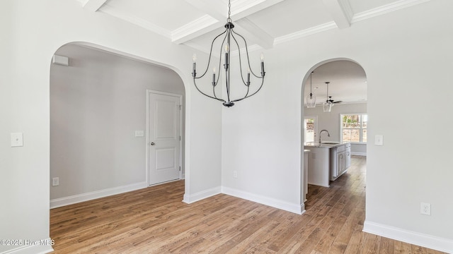 unfurnished dining area featuring a sink, beam ceiling, light wood finished floors, arched walkways, and coffered ceiling