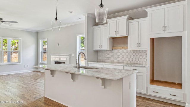 kitchen featuring a kitchen island with sink, light wood-style flooring, ornamental molding, and a sink