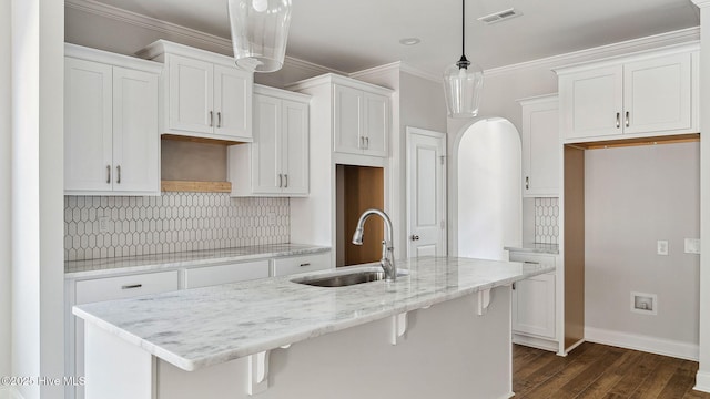 kitchen with a sink, white cabinets, a center island with sink, visible vents, and dark wood-style flooring