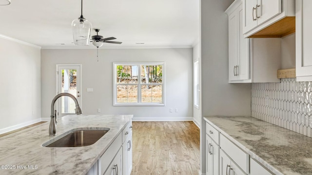 kitchen with a sink, crown molding, light stone countertops, and a ceiling fan