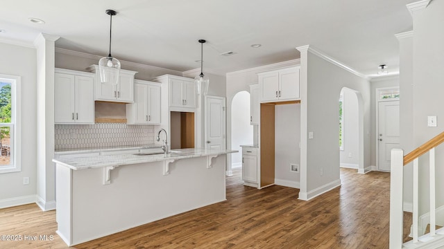 kitchen with a sink, arched walkways, a kitchen island with sink, and wood finished floors