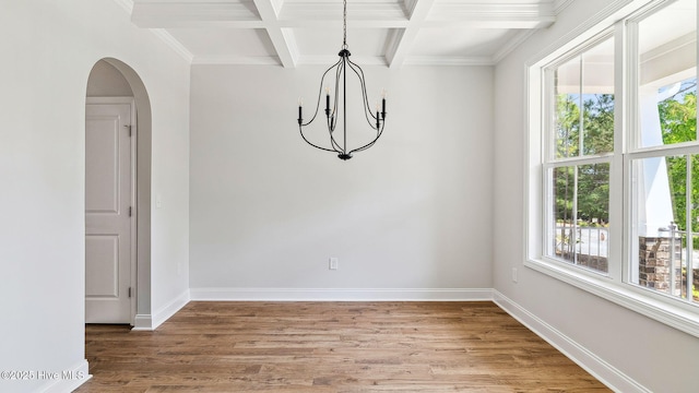 unfurnished dining area featuring a chandelier, beamed ceiling, arched walkways, and light wood-style floors