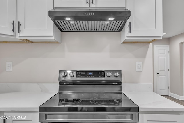 kitchen with stainless steel electric stove, light stone countertops, white cabinetry, and range hood