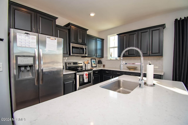 kitchen featuring appliances with stainless steel finishes, decorative backsplash, sink, and light stone counters