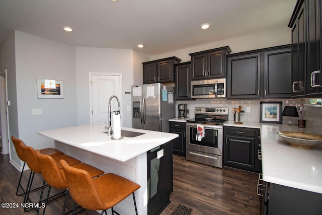 kitchen with a center island with sink, a kitchen breakfast bar, dark hardwood / wood-style floors, sink, and stainless steel appliances