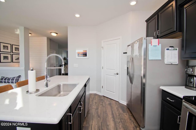 kitchen featuring dark wood-style floors, a center island with sink, stainless steel refrigerator with ice dispenser, light countertops, and a sink