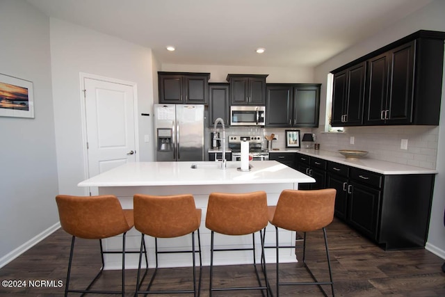 kitchen with appliances with stainless steel finishes, baseboards, decorative backsplash, a kitchen bar, and a center island with sink