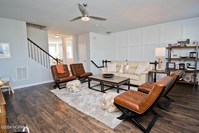 living room featuring a decorative wall, a ceiling fan, wood finished floors, visible vents, and stairway