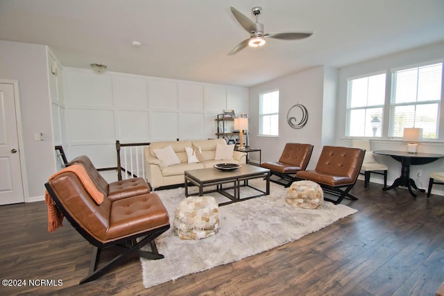 living room featuring a decorative wall, a ceiling fan, and dark wood-type flooring