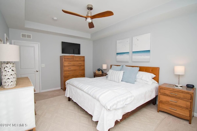 bedroom with a ceiling fan, a tray ceiling, visible vents, and light carpet
