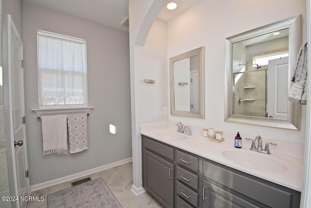 bathroom featuring double vanity, baseboards, a sink, and a shower