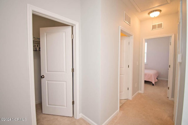 hallway with light colored carpet, baseboards, visible vents, and attic access