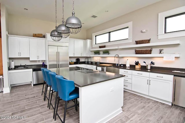 kitchen featuring dark countertops, appliances with stainless steel finishes, open shelves, a sink, and white cabinetry
