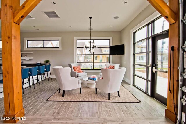 living area featuring a healthy amount of sunlight, an inviting chandelier, light wood finished floors, and visible vents