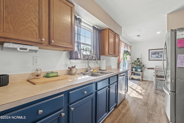 kitchen featuring a textured ceiling, stainless steel appliances, sink, blue cabinetry, and light hardwood / wood-style floors