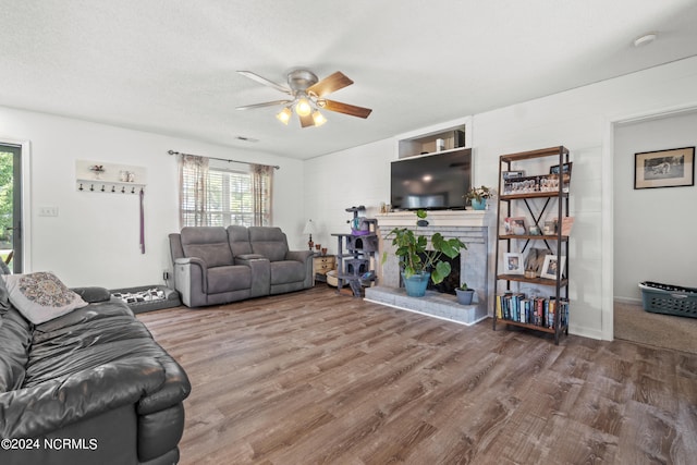 living room with ceiling fan, wood-type flooring, a textured ceiling, and a brick fireplace