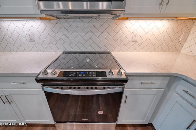 kitchen with dark wood-type flooring, stainless steel electric range, white cabinetry, and backsplash