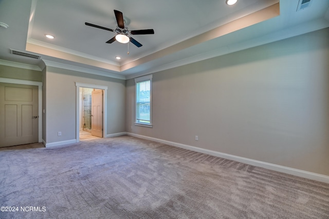 unfurnished bedroom with a raised ceiling, light colored carpet, ensuite bathroom, and ceiling fan