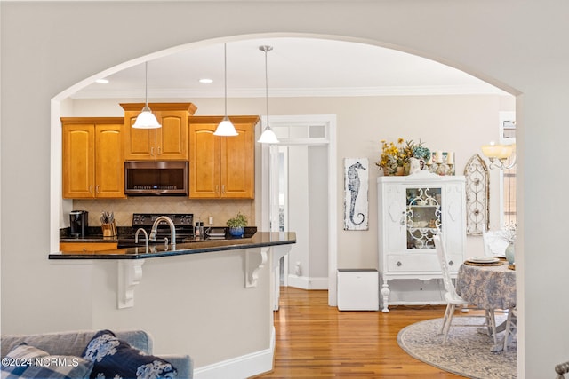 kitchen featuring pendant lighting, tasteful backsplash, appliances with stainless steel finishes, a breakfast bar area, and light hardwood / wood-style floors