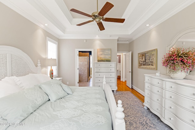 bedroom featuring ceiling fan, light hardwood / wood-style floors, a tray ceiling, ornamental molding, and ensuite bathroom