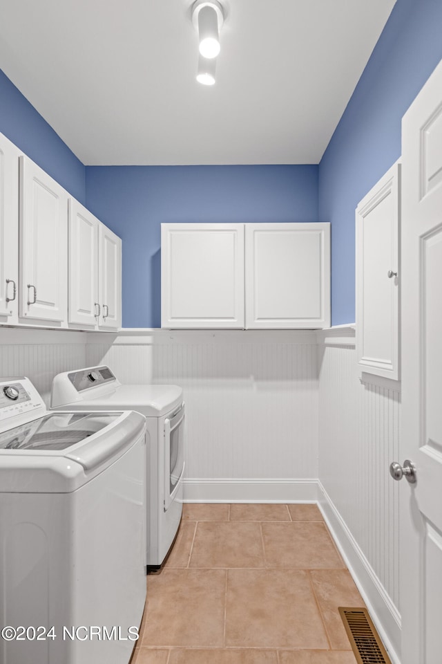 laundry room featuring washing machine and dryer, cabinets, and light tile patterned floors