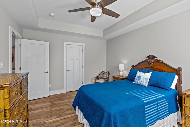 bedroom with a raised ceiling, ceiling fan, and dark hardwood / wood-style floors