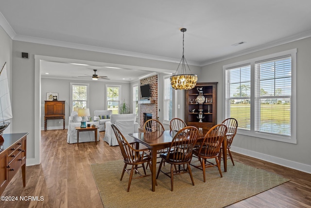 dining area featuring ceiling fan with notable chandelier, a brick fireplace, crown molding, and hardwood / wood-style floors