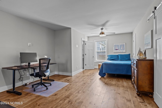 bedroom featuring ceiling fan, light hardwood / wood-style flooring, and a barn door