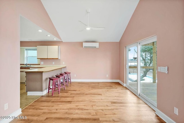 kitchen with white cabinetry, a kitchen breakfast bar, kitchen peninsula, light hardwood / wood-style flooring, and a wall mounted air conditioner