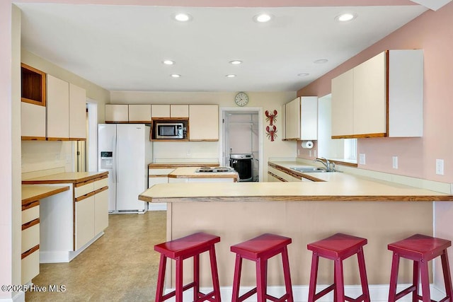 kitchen featuring a kitchen bar, white fridge with ice dispenser, kitchen peninsula, and sink