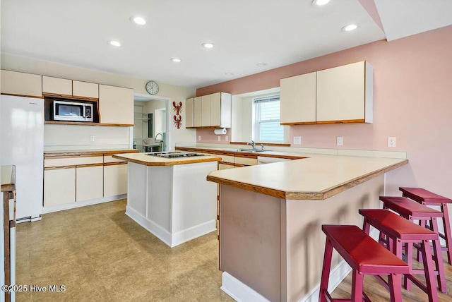 kitchen with black gas stovetop, a kitchen island, white fridge, sink, and kitchen peninsula