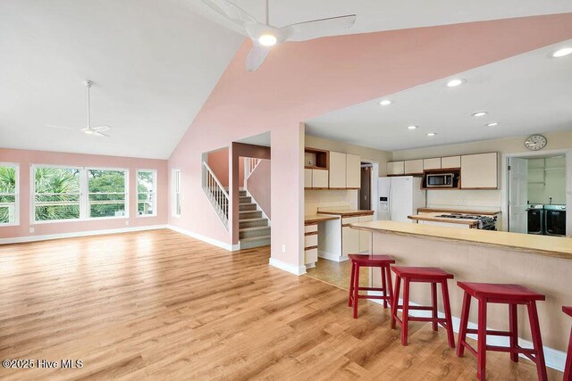 kitchen with ceiling fan, a breakfast bar, stove, light wood-type flooring, and white fridge with ice dispenser