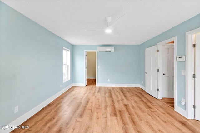 unfurnished bedroom featuring ceiling fan, light hardwood / wood-style floors, a spacious closet, and a wall unit AC