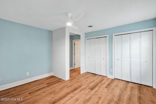 unfurnished bedroom with ceiling fan, light wood-type flooring, and multiple closets