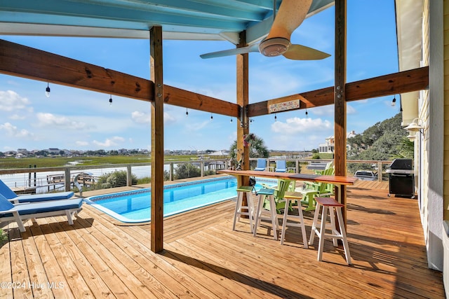 view of pool with ceiling fan, area for grilling, and a deck with water view