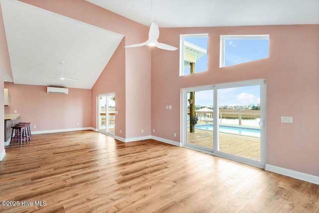 unfurnished living room with light wood-type flooring, ceiling fan, a wall mounted AC, and a high ceiling