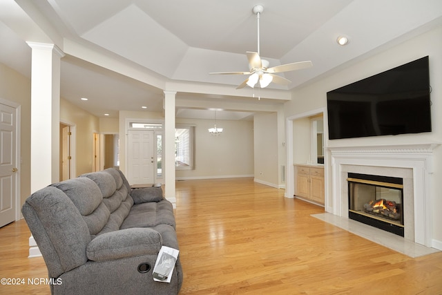 living room with ceiling fan with notable chandelier, light wood-type flooring, a fireplace, and decorative columns