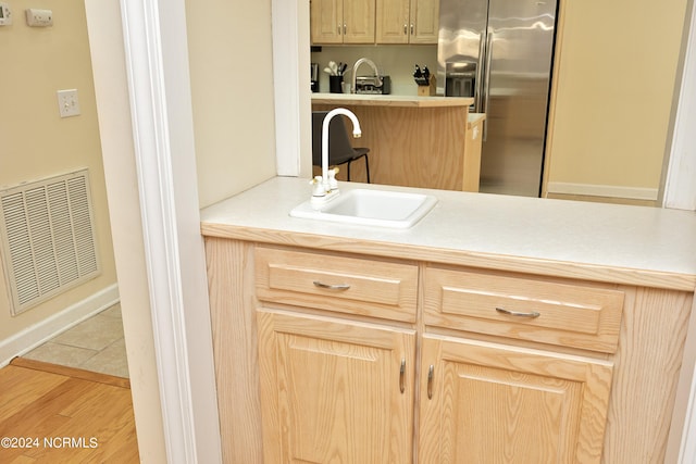 kitchen with light brown cabinetry, stainless steel fridge with ice dispenser, sink, and light hardwood / wood-style floors