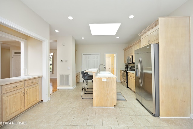 kitchen with a kitchen island with sink, stainless steel appliances, sink, a breakfast bar area, and light brown cabinetry