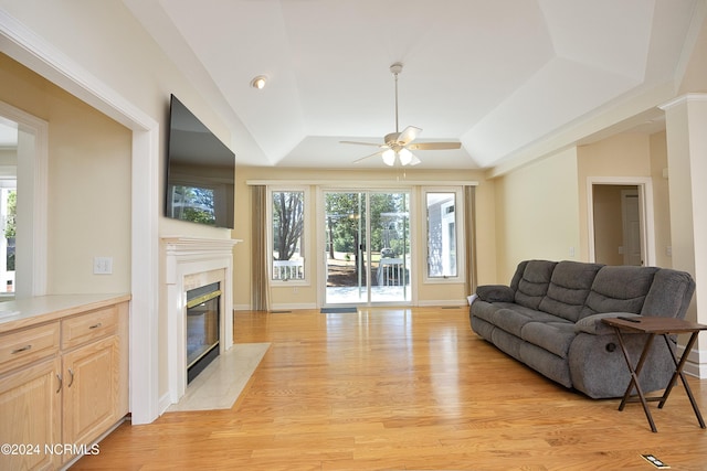 living room with ceiling fan, light wood-type flooring, a premium fireplace, and a tray ceiling