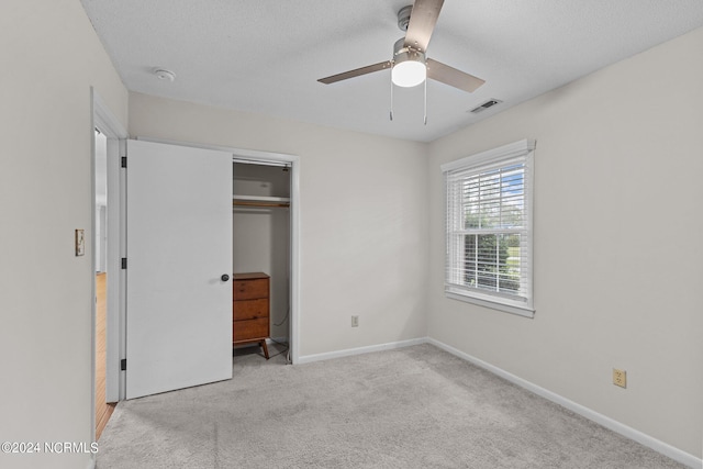 unfurnished bedroom featuring light carpet, a textured ceiling, a closet, and ceiling fan