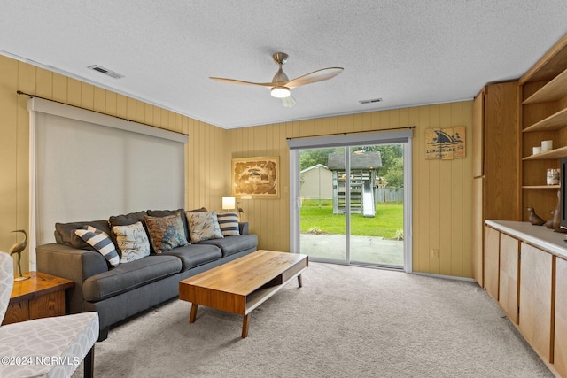 living room featuring wooden walls, light carpet, a textured ceiling, and ceiling fan