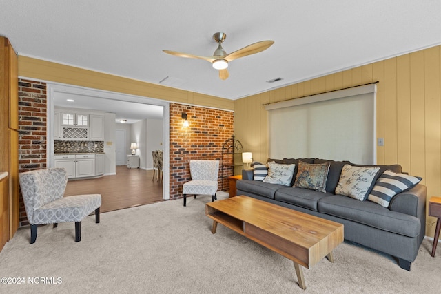 carpeted living room with ceiling fan, wood walls, and ornamental molding